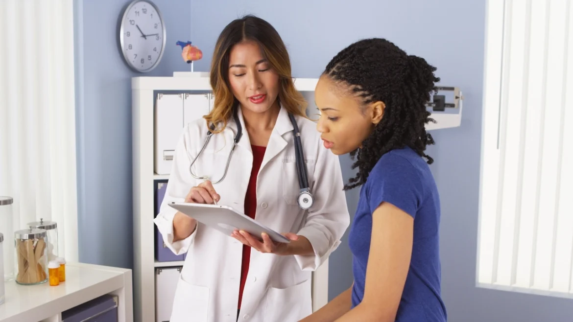 Image of Asian doctor holding a tablet while talking with an African American patient