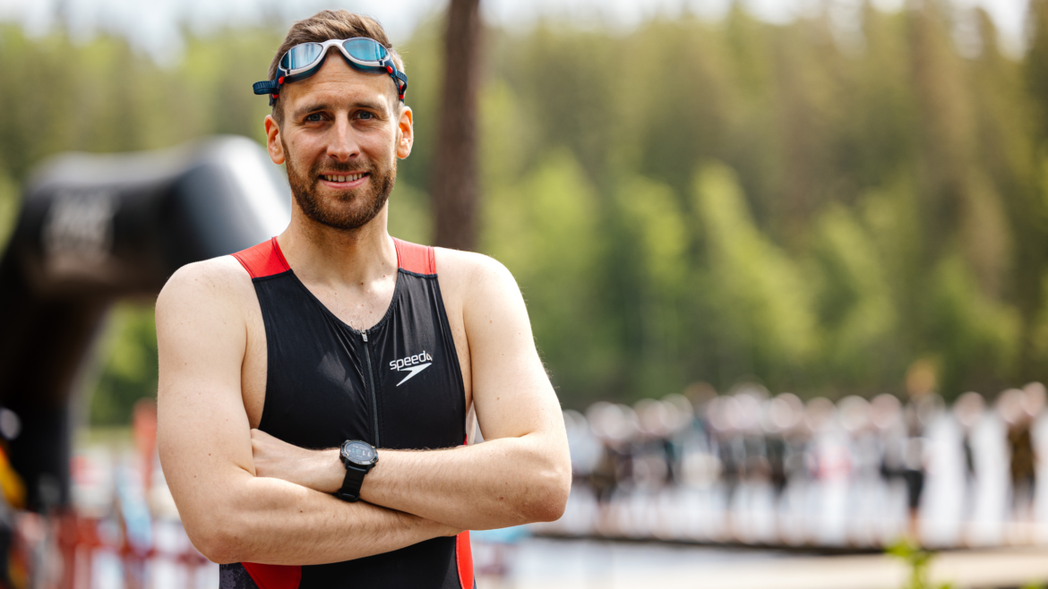 man standing in triathlon kit with goggles on head and arms crossed, looking at the camera