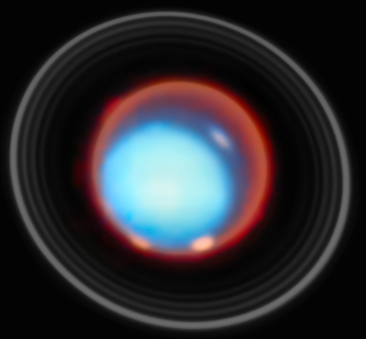 This image shows the planet Uranus set against the blackness of space. The planet appears as a smooth, bright cyan disc at the center, its atmosphere reveals soft, hazy tones of blue. Surrounding the planet is a vivid reddish glow, forming a diffuse halo that contrasts strongly with the cool blue of the planetary disc. Encircling Uranus are several thin, concentric rings, visible as pale gray arcs. Subtle variations in brightness can be seen across the planet’s face, with slightly brighter patches near the limb, hinting at atmospheric structure.