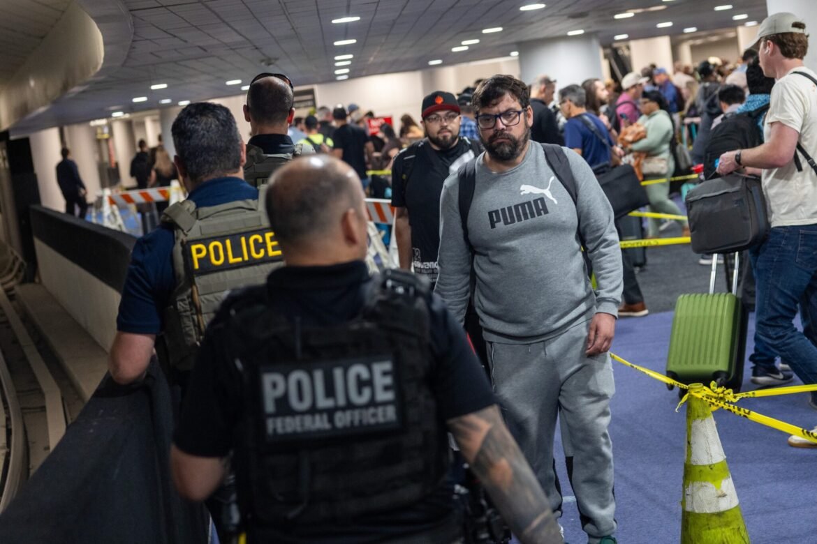 A traveler looks at Immigration and Customs Enforcement agents as they walk around the end of the line at Terminal E at George Bush Intercontinental Airport on March 24, 2026 in Houston, Texas. Travel disruptions continue as hundreds of TSA agents quit or work without pay during a partial government shutdown and ICE agents are sent to some airports to assist. (Photo by Antranik Tavitian/Getty Images)