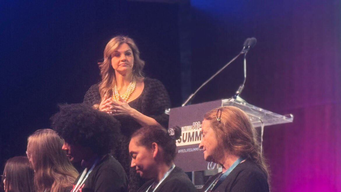 Anti-abortion organizer Abby Johnson spoke at Students for Life of America’s annual National Pro-Life Summit on Jan. 24, 2026, behind former abortion clinic workers wearing “Make Abortion Murder Again” T-shirts. “I don’t think we’re going to hug and kiss our way out of this baby murder,” she told the student activists. (Photo by Sofia Resnick/States Newsroom)&nbsp;