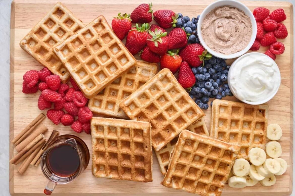 pile of waffles on a cutting board with fruit, cinnamon butter and syrup for Mother