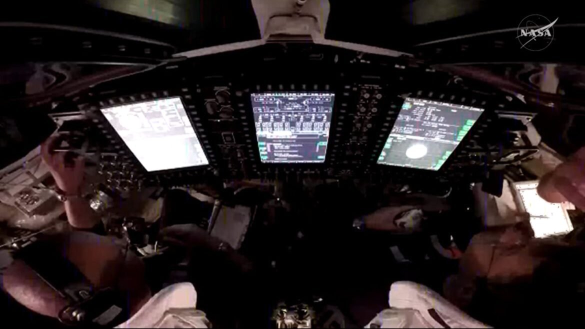 A look into a dark cockpit with three bright white computer screens