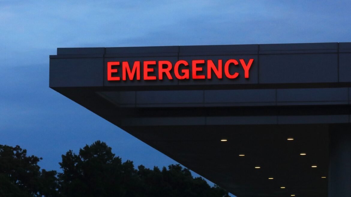 A close up of a hospital overhang with glowing red letters spelling the word "emergency."