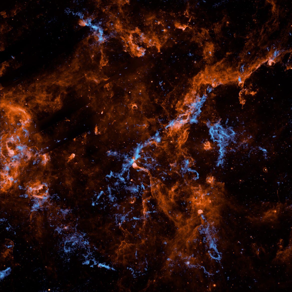 Wispy filaments of vibrant orange and electric blue cosmic dust and gas weave through a dark, star-studded expanse of outer space, creating a chaotic and intricate web of celestial matter.