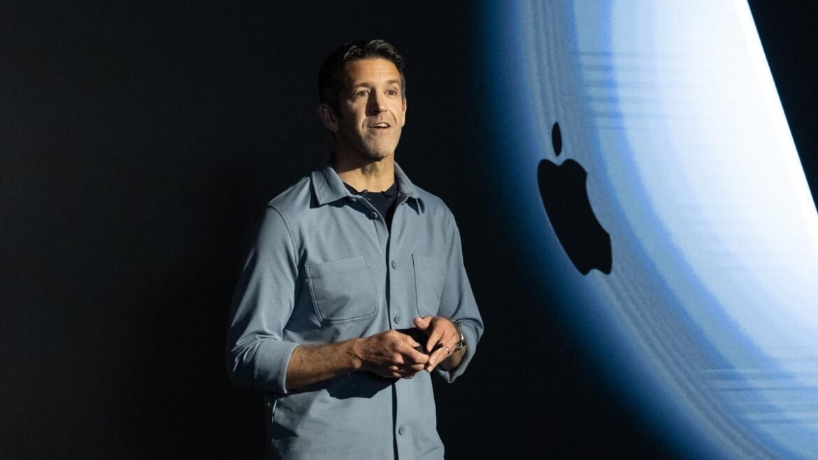 Current Senior Vice President John Ternus stands in front of an Apple logo while on stage.
