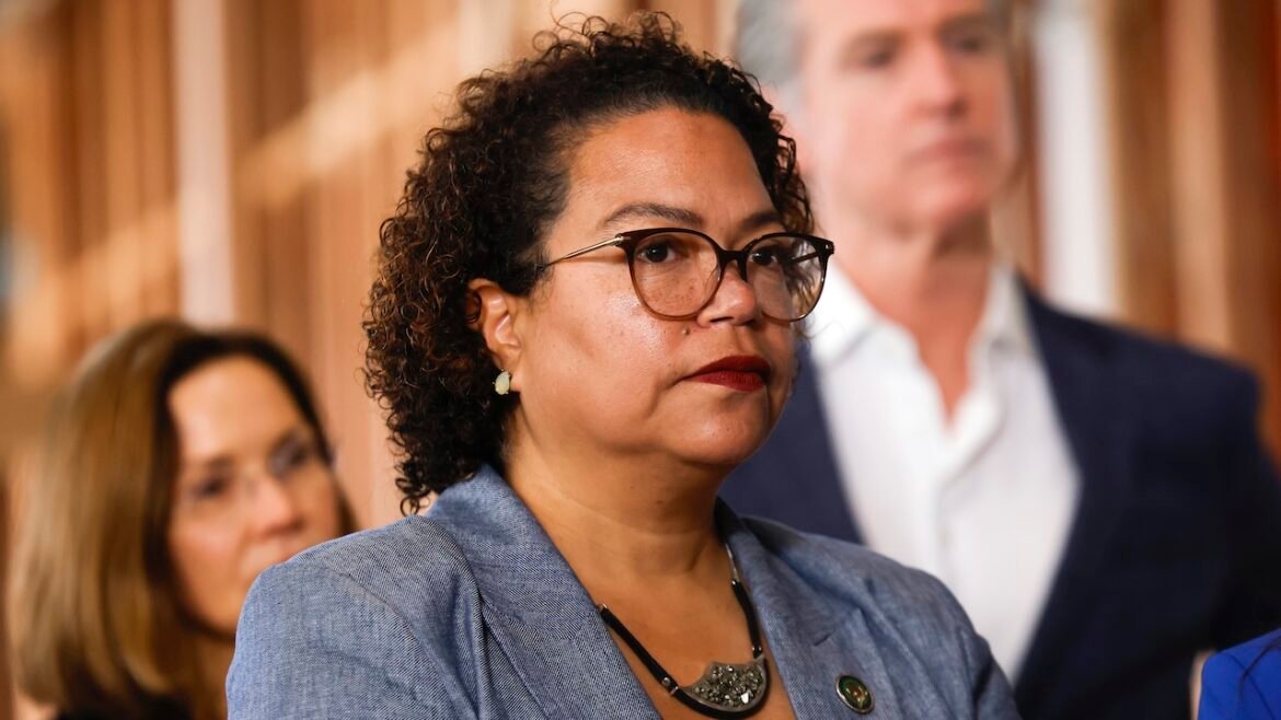 California Assemblymember Mia Bonta looks on as Gov. Gavin Newsom stands in the background.