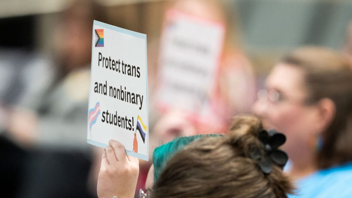 A person holds a sign reading, "Protect trans and nonbinary students!"