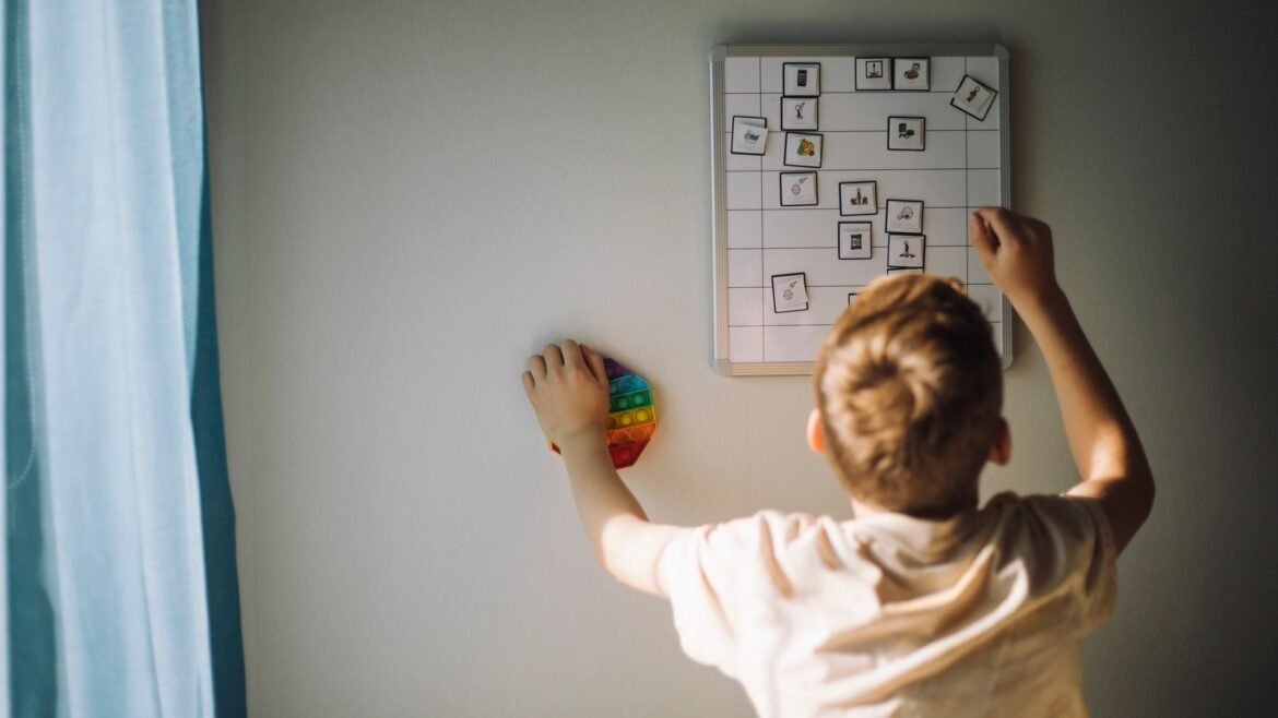 A boy with blond hair reaches up to fix a weekly calendar.