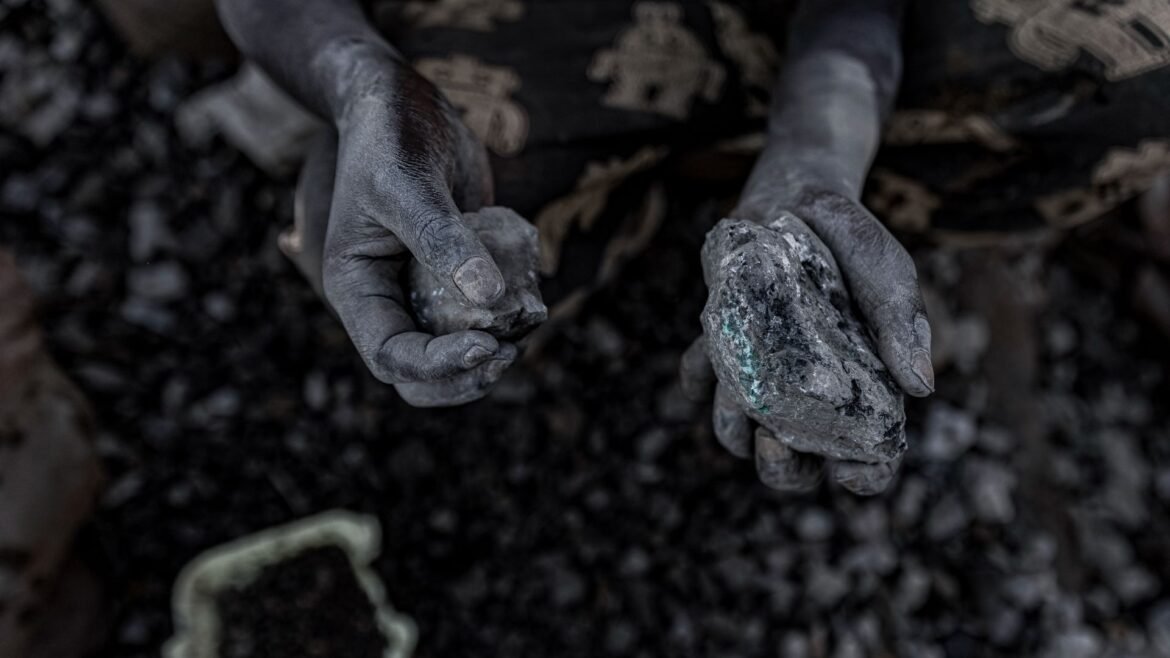 A pair of chalk covered hands hold small stones full of cobalt over a pile of blurry dark stones in the background.