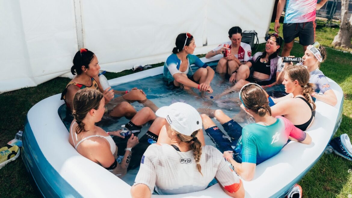 A group of pro female triathletes sit in a children's inflatable pool filled with water and ice to recover after a triathlon.