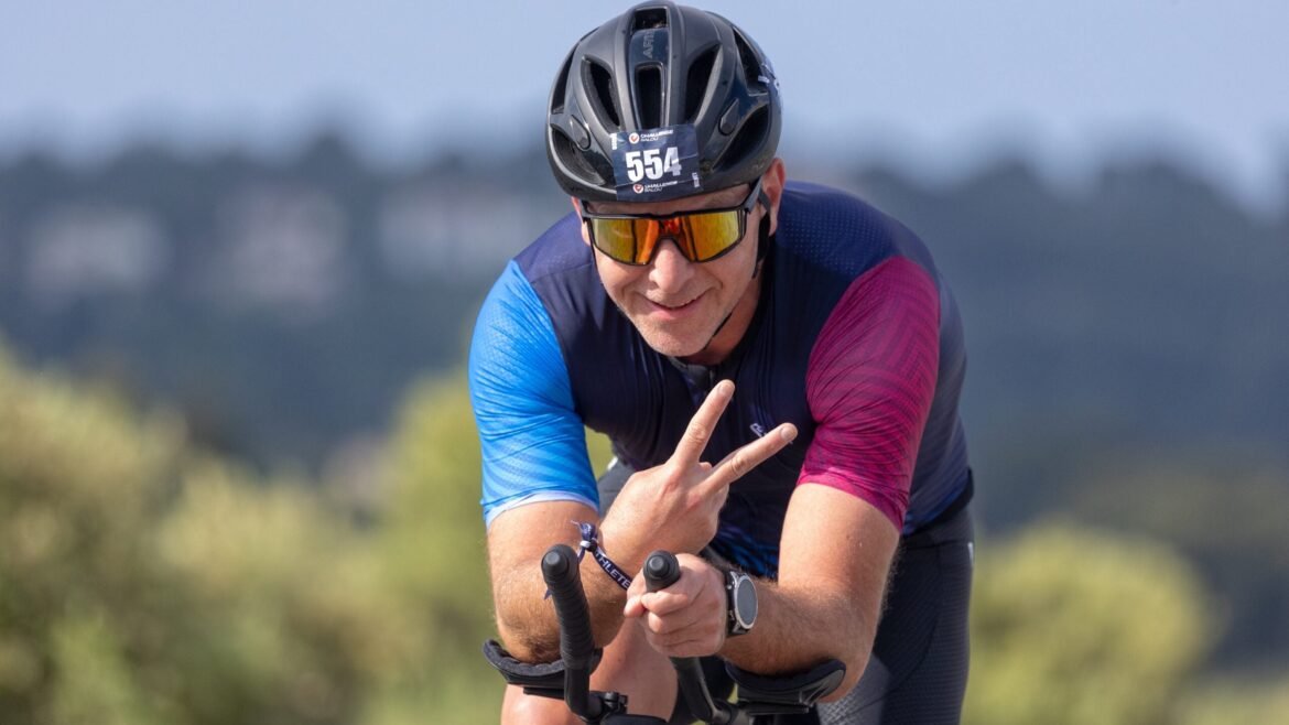 An athlete rides a triathlon bike and puts up to fingers, signifying zone 2 for triathletes.