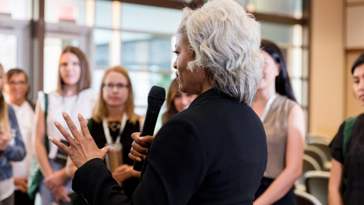 older woman with a microphone addresses a group of people
