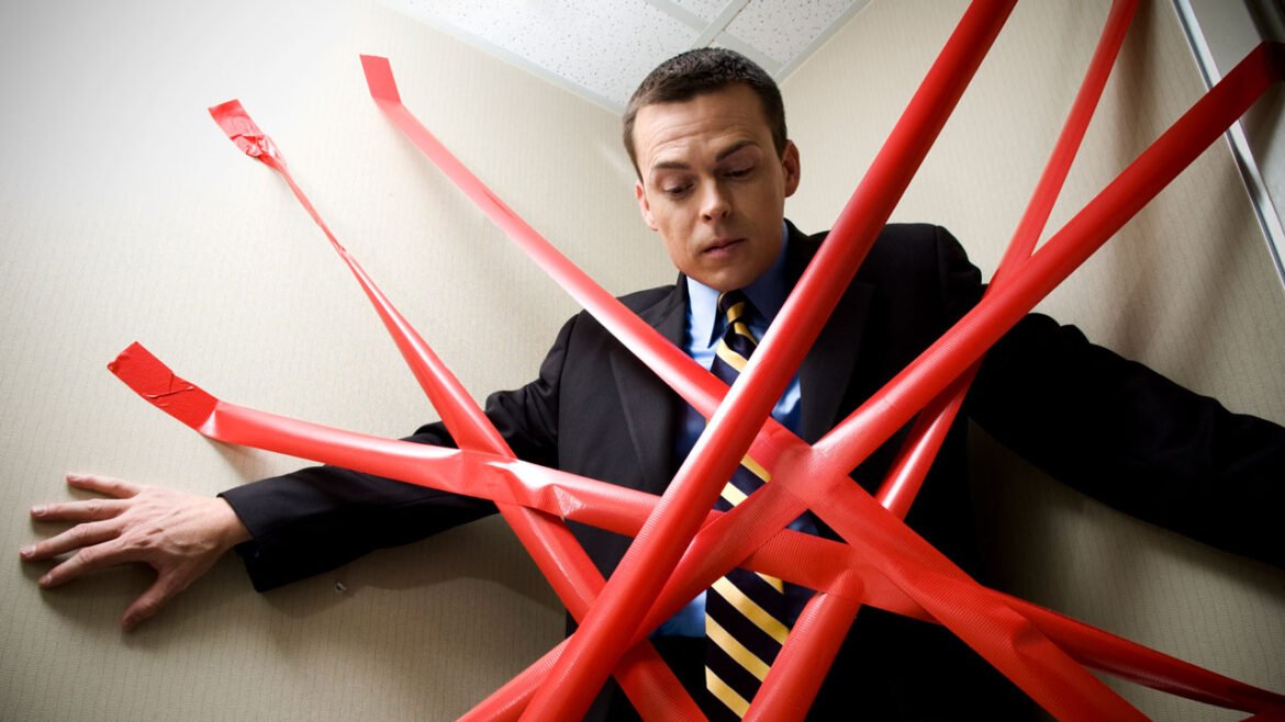 Man in a suit pinned in a corner by numerous strips of red tape.