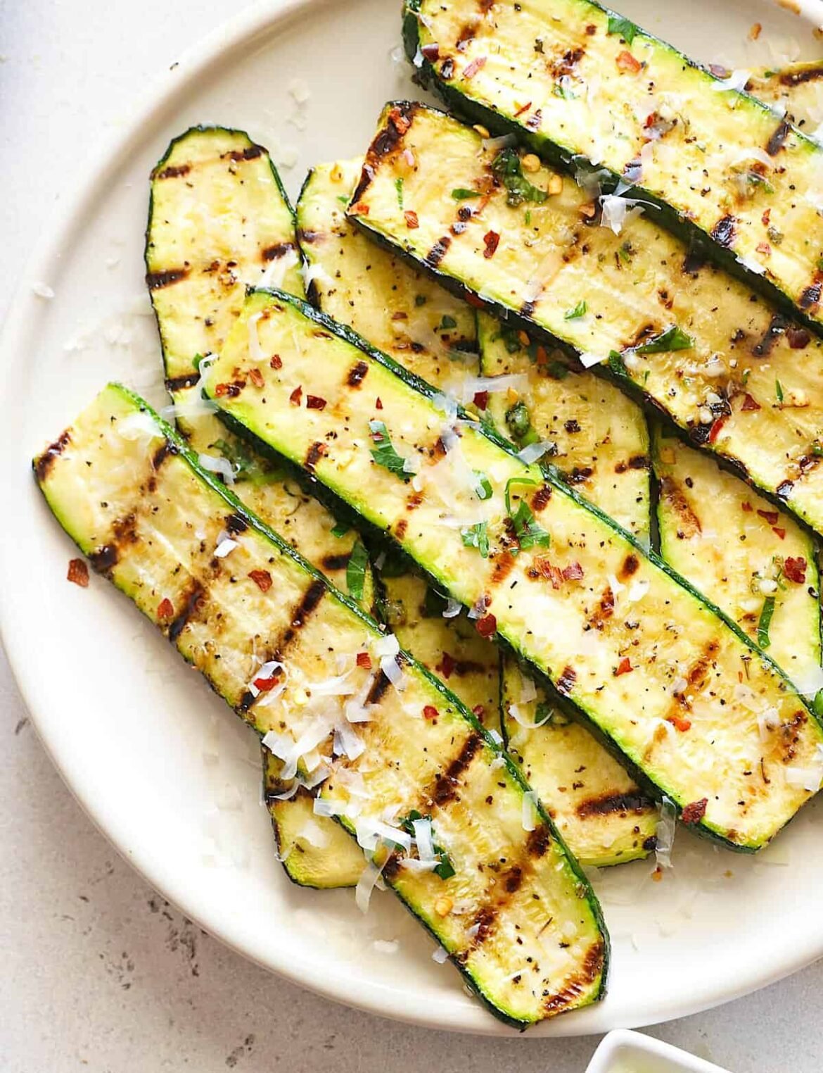 Freshly grilled zucchini on a white platter waiting to be sprinkled with Parmesan and devoured.