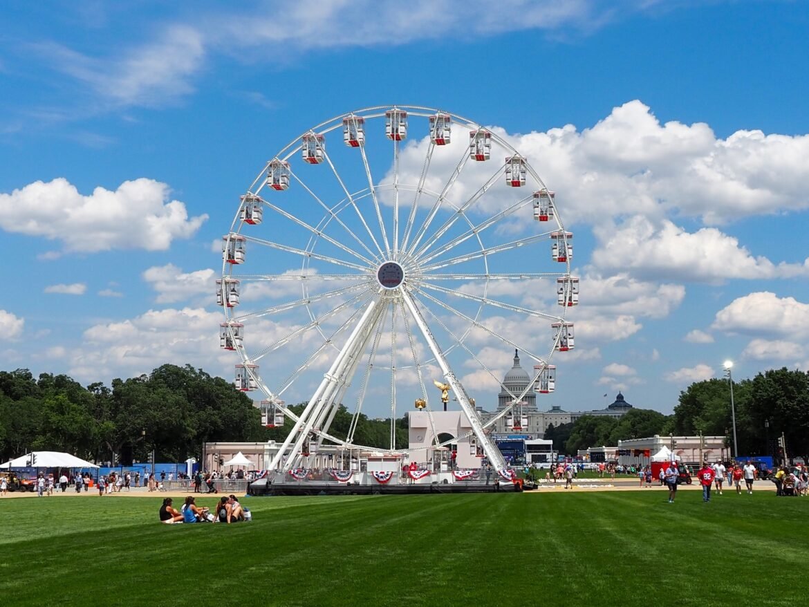Attendees sit in the grass in front of the Ferris wheel at the Trump administration's Freedom 250 Great American State Fair on the National Mall on Thursday, June 25, 2026. (Photo by Ashley Murray/States Newsroom)