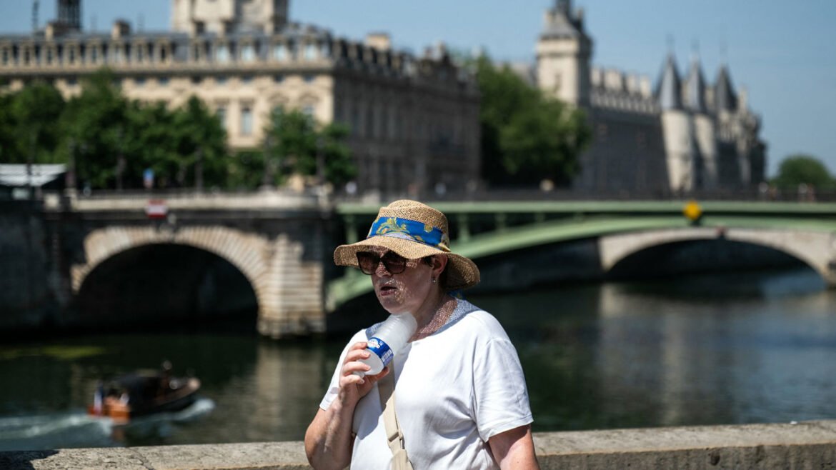 A woman with a hat cools off with a cold bottle of water on the Seine riverside with the Paris commercial court (L) and the Conciergerie buildings and the Pont Notre Dame in the background as France experiences a heat wave in Paris, France, on June 21, 2026.