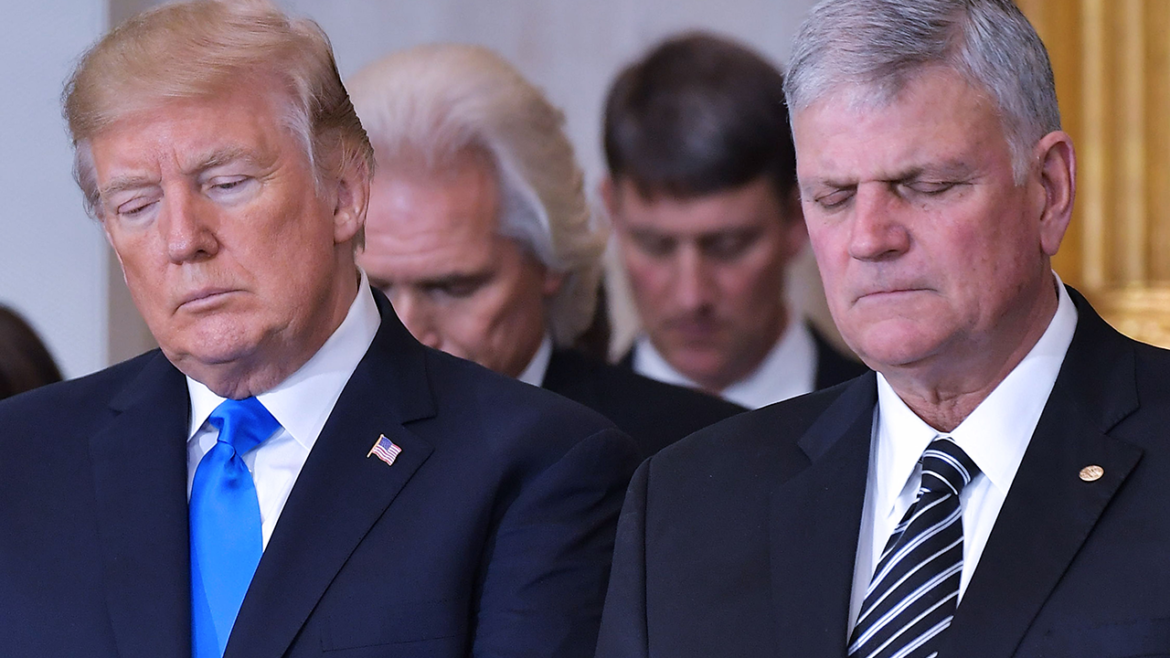 Donald Trump stands next to Franklin Graham in the US Capitol Rotunda, both bowing their heads in prayer.