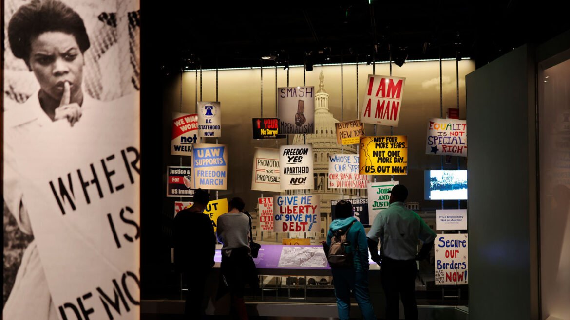 Visitors stand in front of an exhibit of protests signs at National Museum of American History.