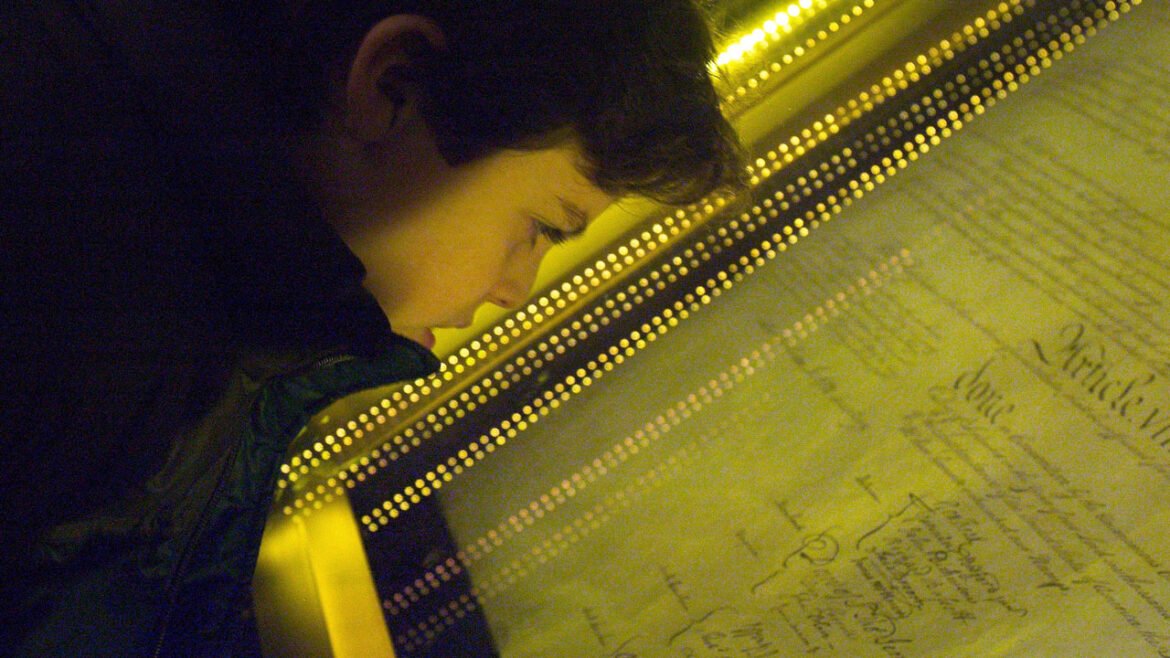 Close-up of a boy looking through a glass frame at the U.S. Constitution.