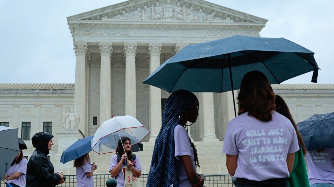 A group of young women stand around the Supreme Court with umbrellas.