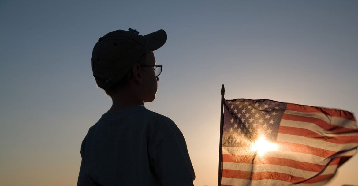 Silhouette of a boy with a setting sun shining through an American flag.