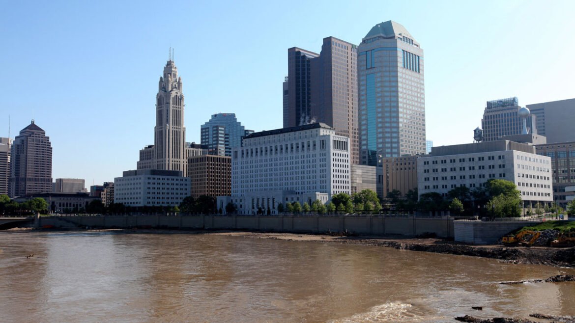 Downtown city skyline of Columbus, Ohio with river and blue sky in the background.