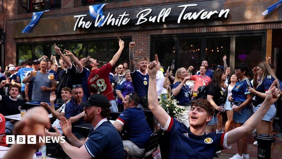 A group of Scotland fans cheer outside a bar called The White Bull Tavern. 