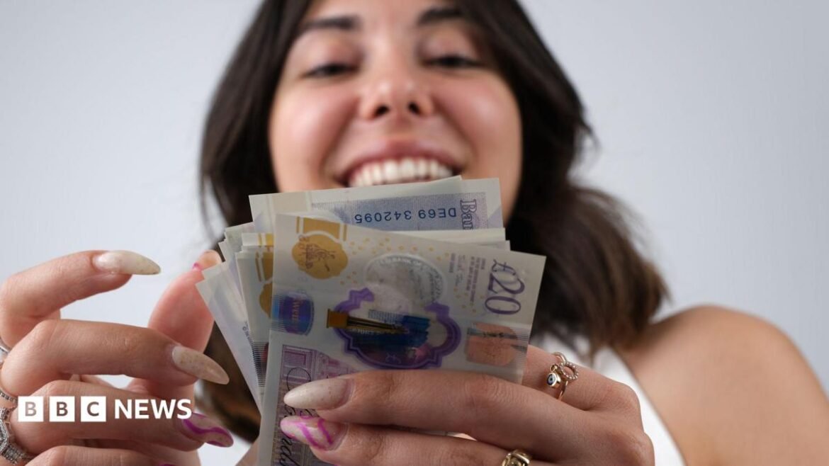 Smiling woman looks at a wad of banknotes with the camera looking from below.