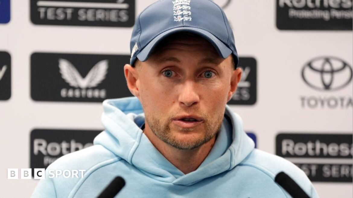 Joe Root speaks to the media with sponsors boards behind him