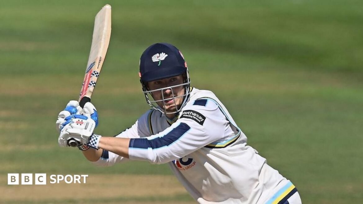 James Wharton, wearing a Yorkshire batting helmet and cricket whites, plays a shot