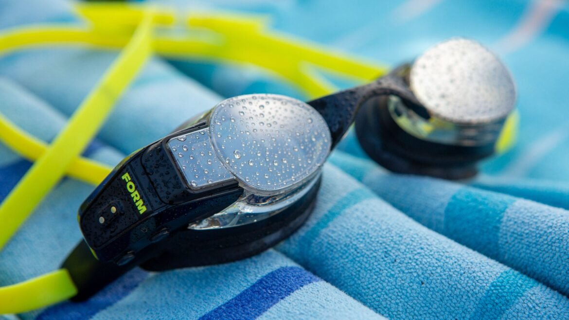 pair of Form Smart Swim 2 LT goggles with fluorescent strap on top of blue striped towel