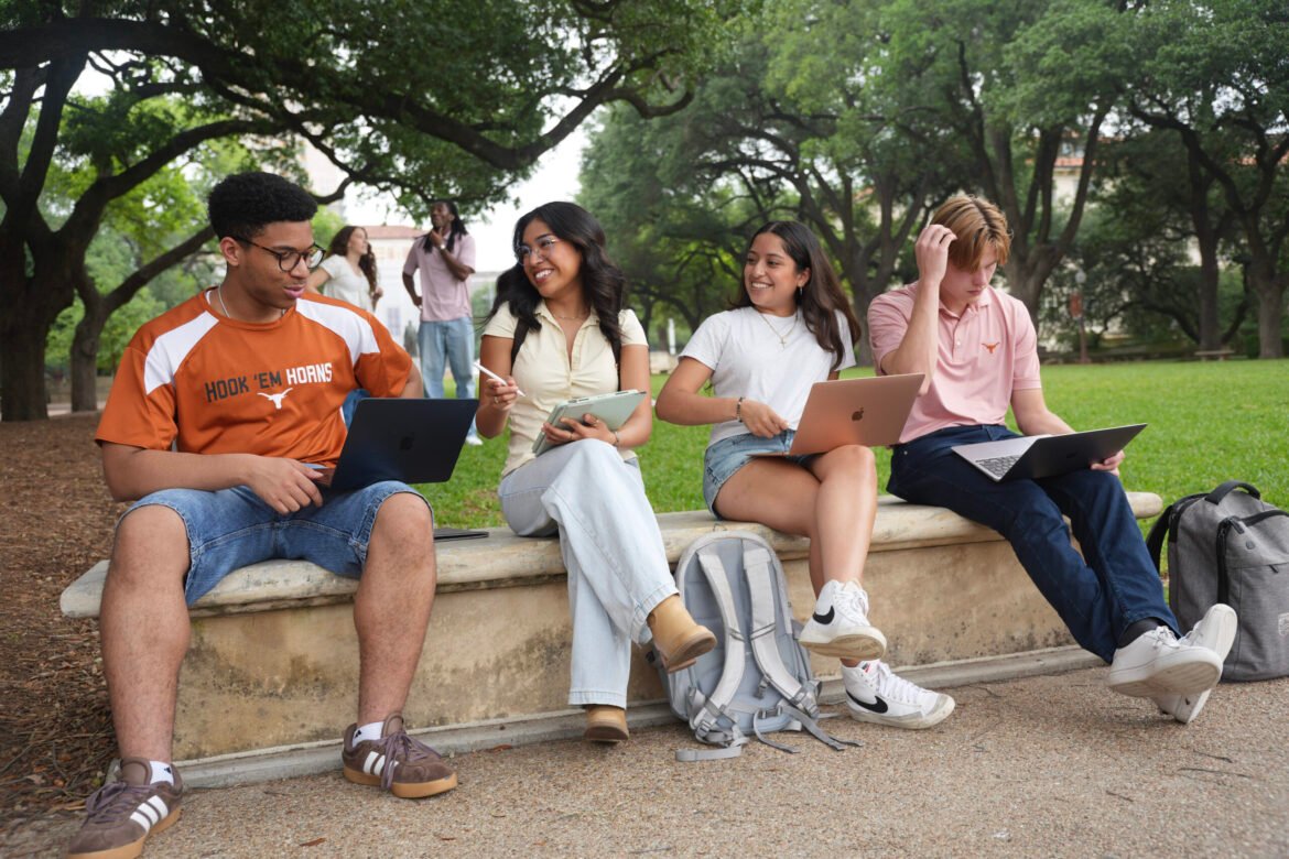 image of students sitting on a bench on their laptops