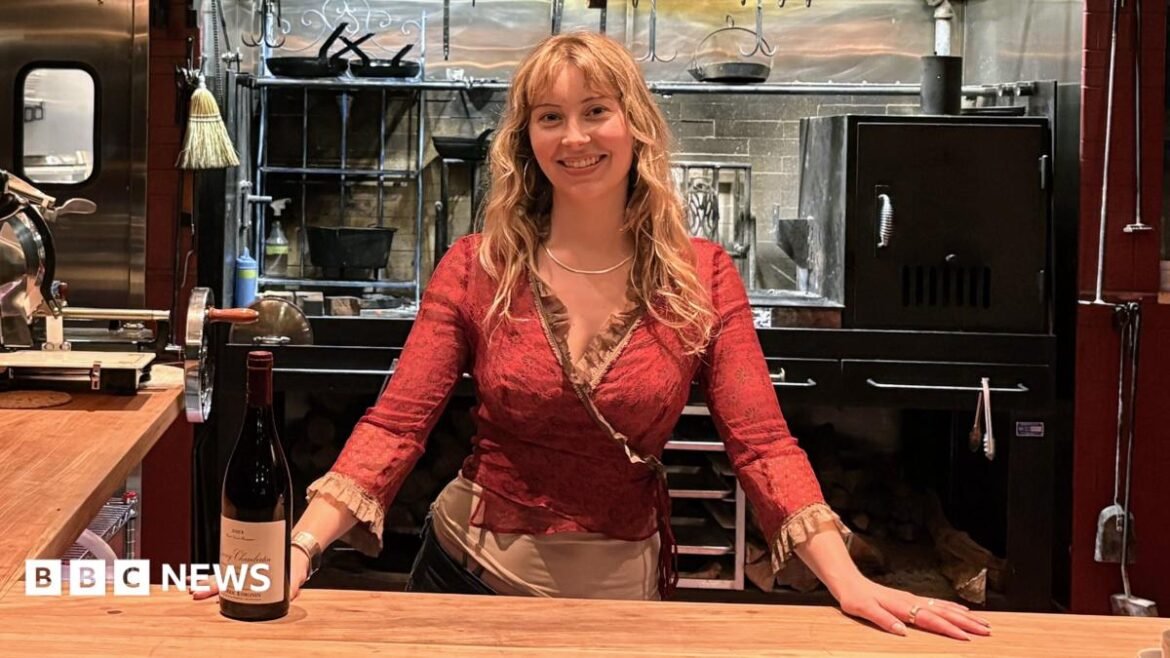 Caroline Kraetzer stands behind a bar, with her hands on the counter.