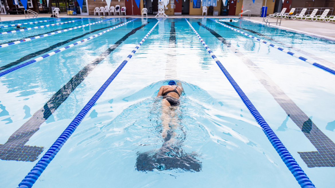 woman in swimsuit and swim cap swims away from the camera in the middle of a pool lane