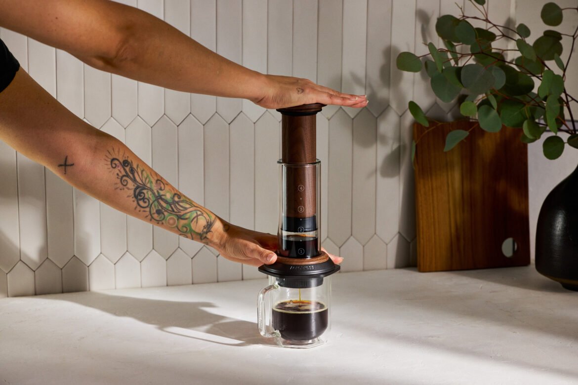 A hand pushing down on the walnut AeroPress brewer.