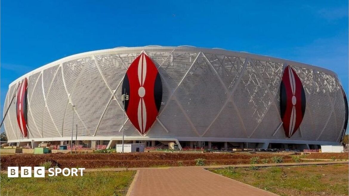 Exterior of a football stadium showing three Kenyan shields in red, white and black on top of a white wrap around