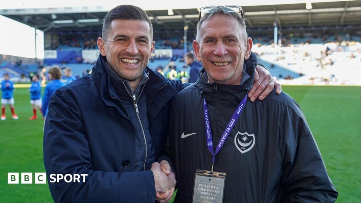 Alan Knight standing by the side of the Fratton Park pitch shaking manager John Mousinho's hand whilst Mousinho has his left arm around Knight's shoulders in embrace, both smiling