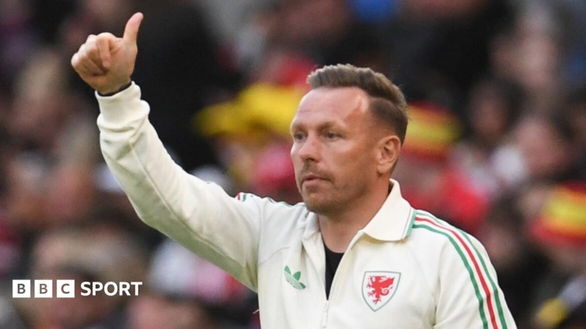 Craig Bellamy on the touchline in a cream Wales top holds a thumb up