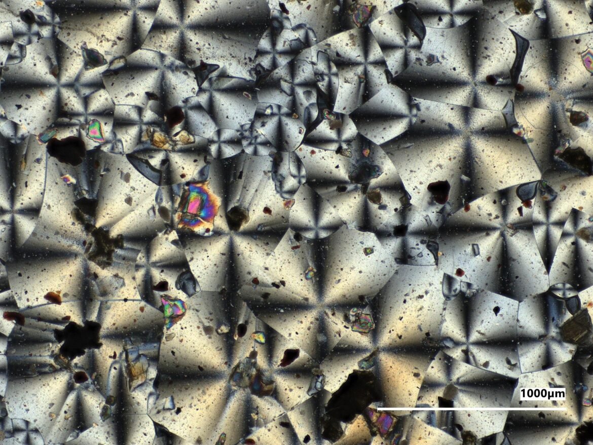 A microscopic view of the kaleidoscope-like crystal structures of two NASA-made material samples, a gray sample on the left and a reddish sample on the right.