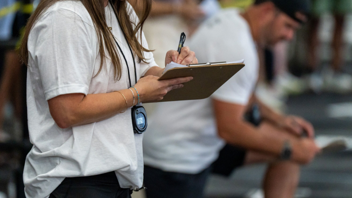 Coach Wearing A Stopwatch And Writing On Her Clipboard To Assess Athlete Data, Implementing Coaching Systems.