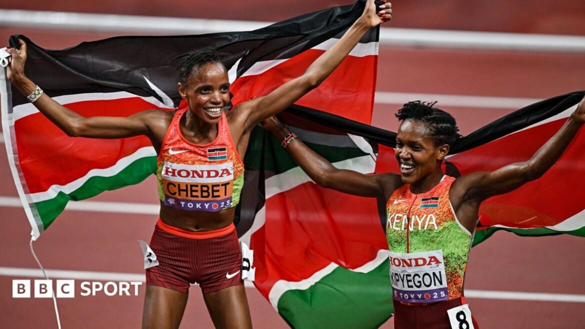Beatrice Chebet and Faith Kipyegon, wearing orange, green and maroon Kenyan running kit, hold Kenyan flags behind them as they celebrate on a terracotta-coloured running track