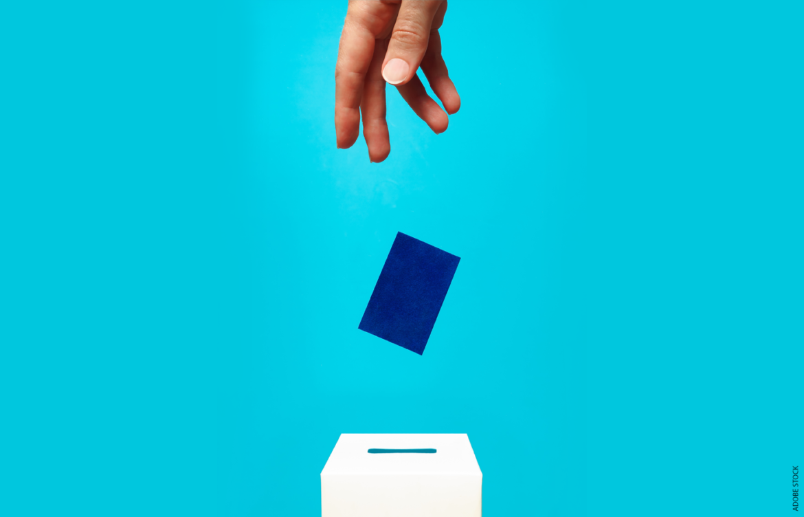 A hand dropping a blue ballot into a ballot box