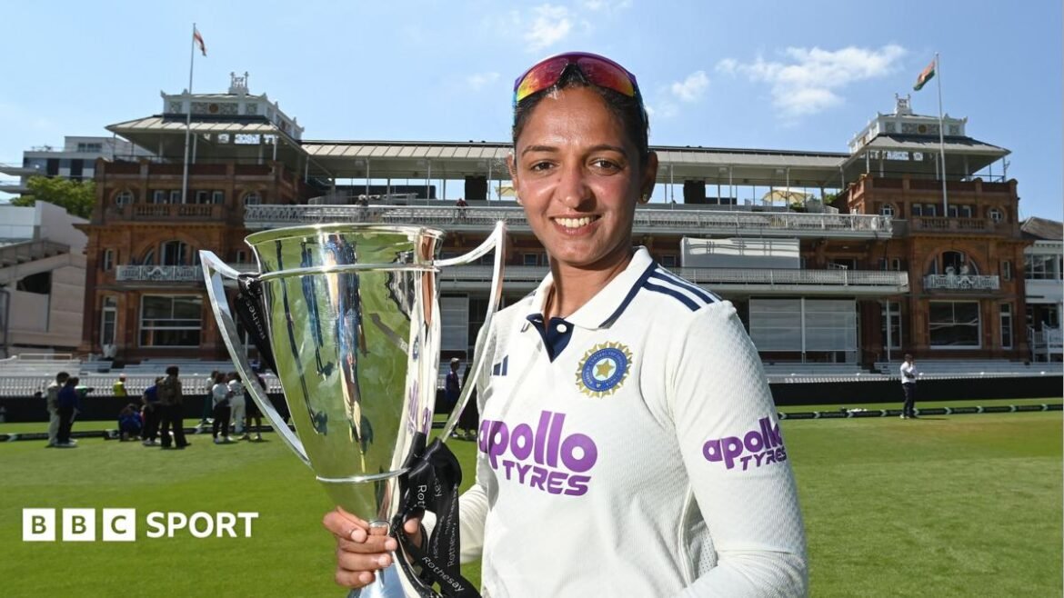 Harmanpreet Kaur, wearing cricket whites and holding a trophy, standing in front of the Lord's pavilion