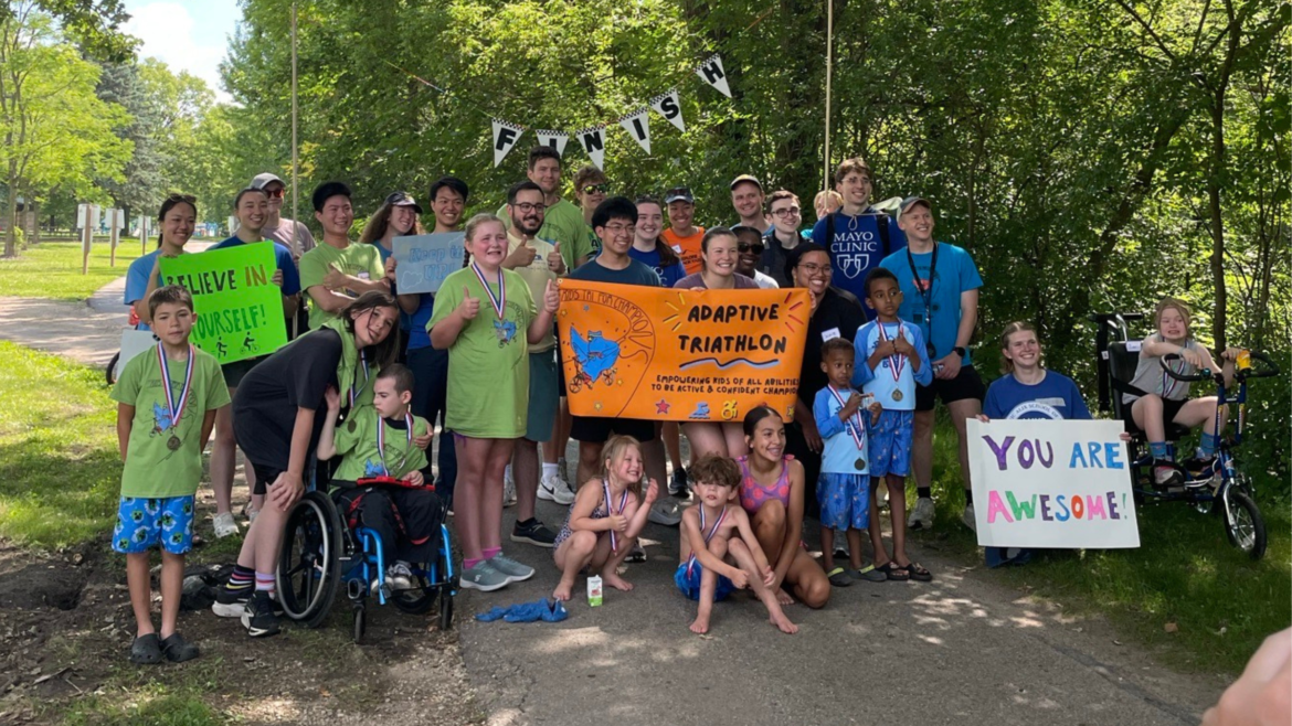 group of kids with disabilities and race volunteers smiling at the finish line of an adaptive kids triathlon