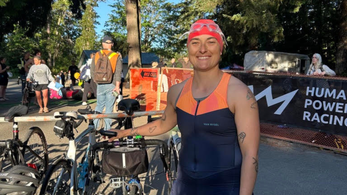 age-group triathlete smiling and standing in tri kit and swim cap with bike before race start